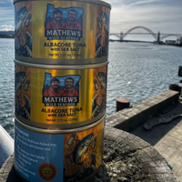 Three cans of Albacore Tuna with Sea Salt by Mathews Wild Seafood in front of the Yaquina Bay Bridge in Newport, Oregon.